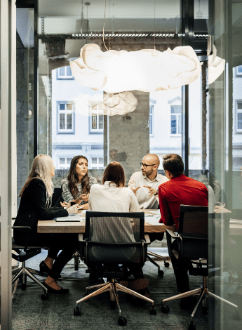 The image is of a group of people sitting around a conference table having a discussion 